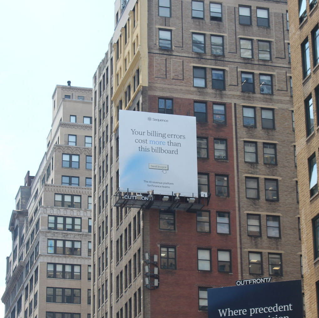 The campaign on a building-mounted board in New York, seen from street level between two office blocks.